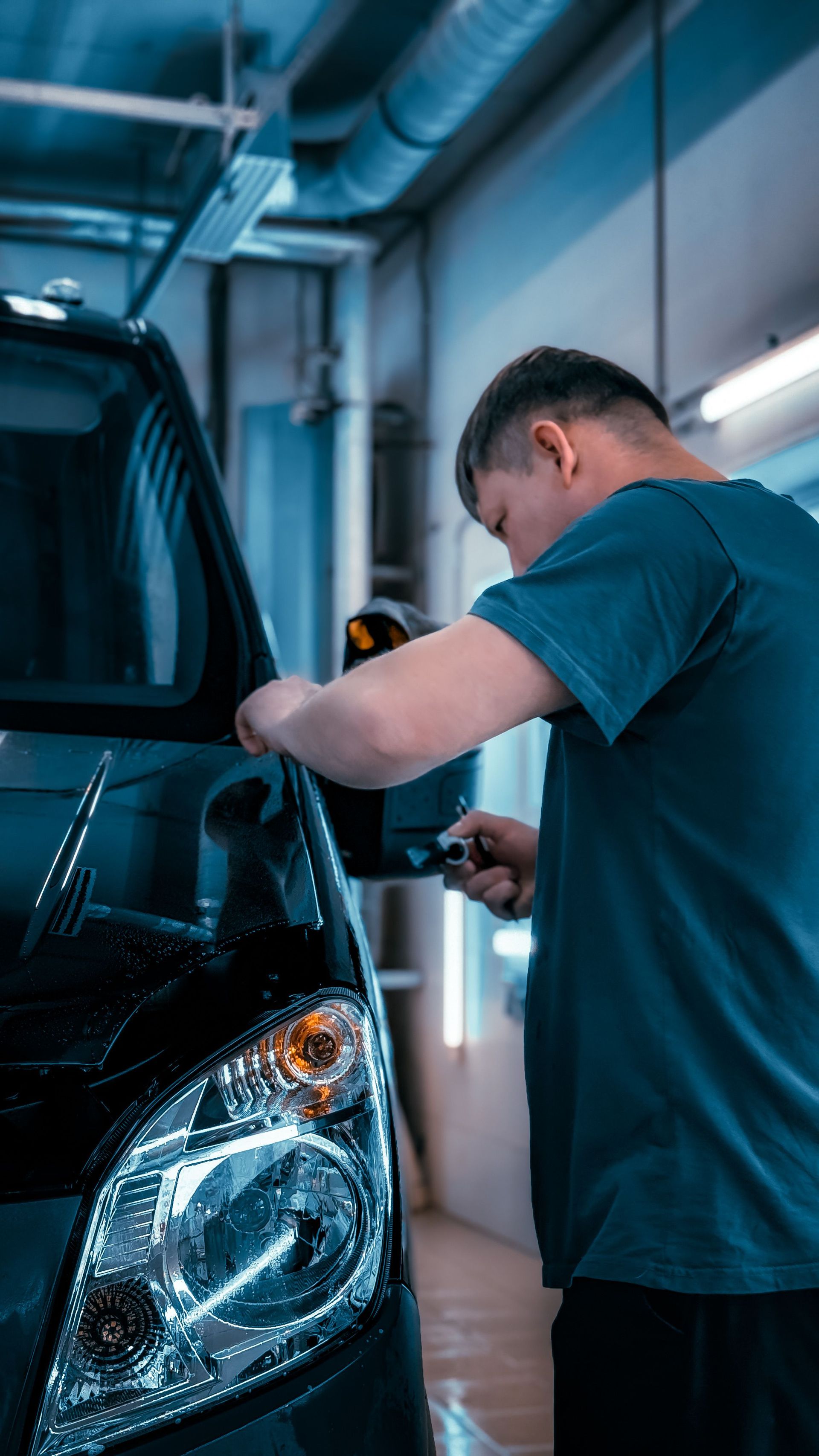 A mechanic focuses on fixing a car's side mirror in a well-lit garage.