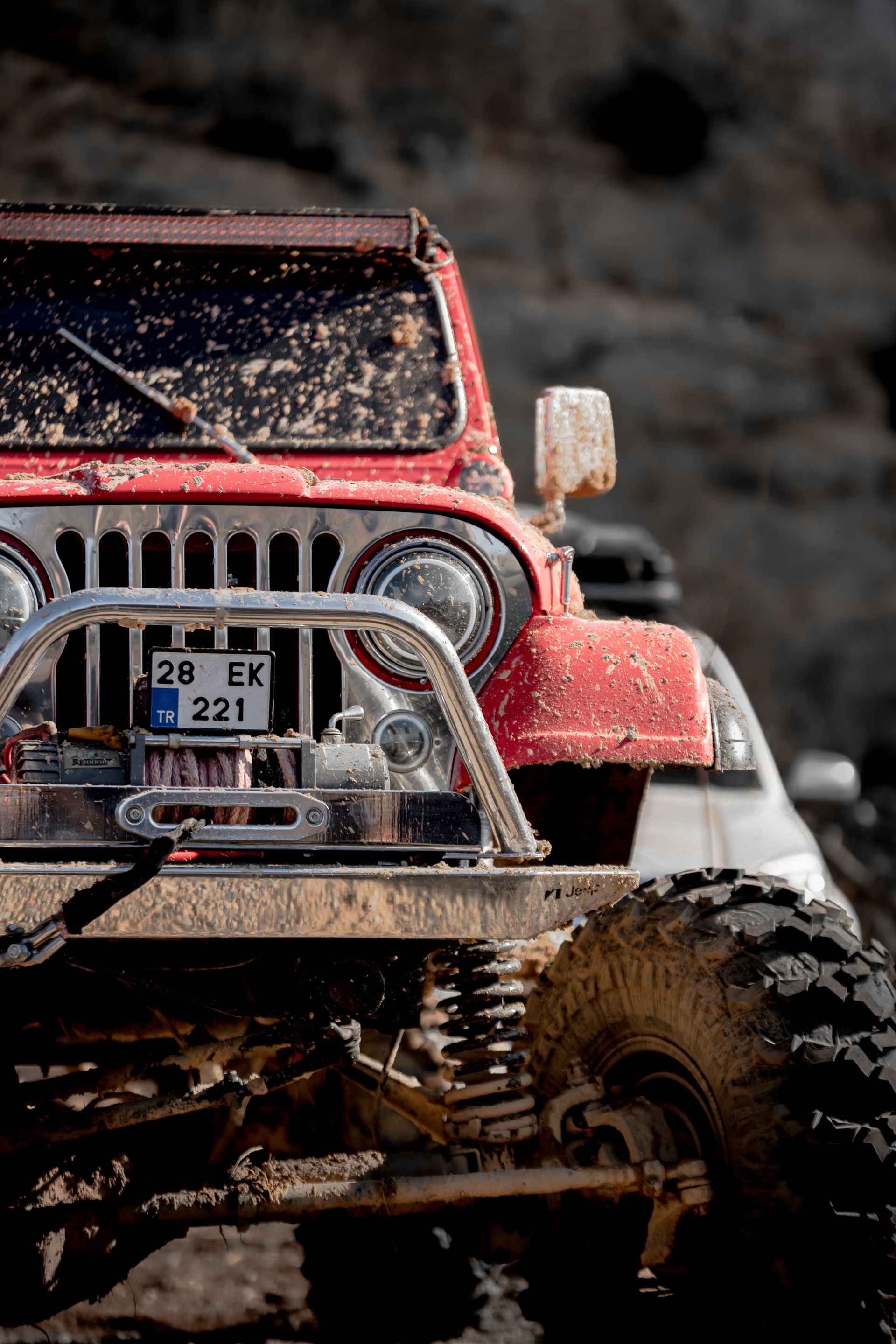 Close-up of a red off-road vehicle covered in mud, showcasing adventure and ruggedness.